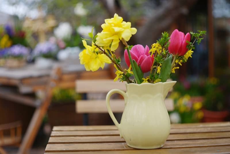 A pitcher of colorful spring flowers on a wooden table.