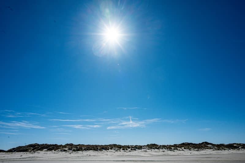 Sun shines in clear blue sky above sandy dunes.