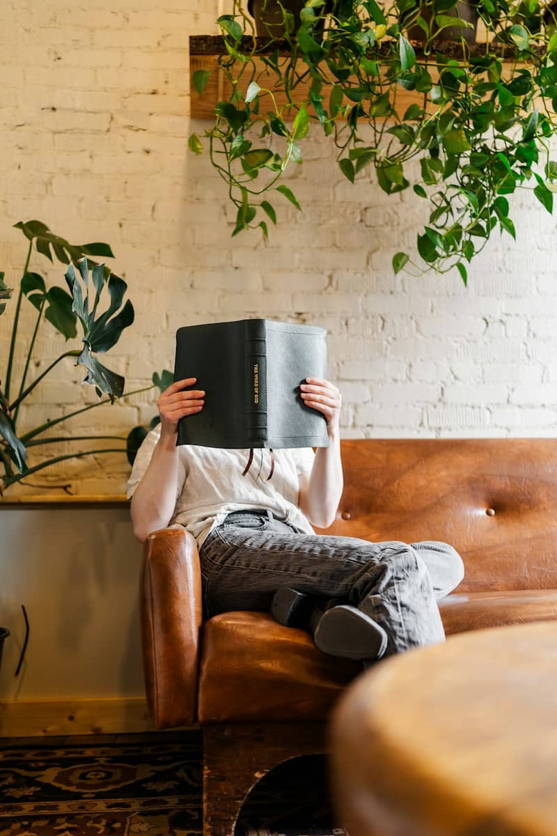 A person sitting on a leather sofa reading a black book in a room