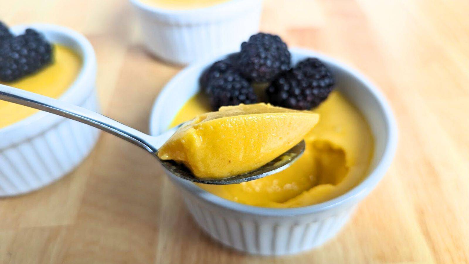 Spoon scooping out mango custard from a ramekin with blackberries.