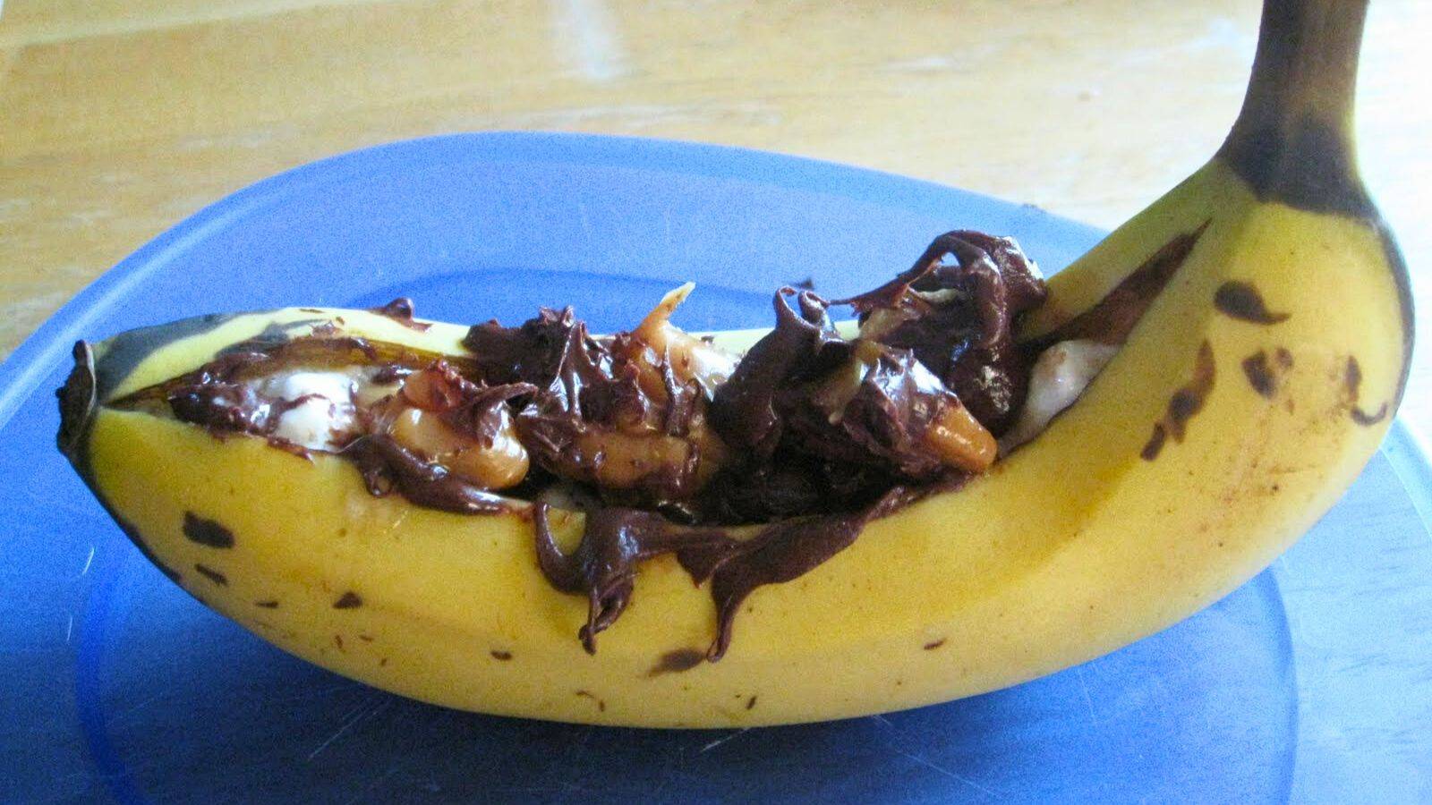 A grilled and stuffed banana sits on a blue plate on a wooden table.
