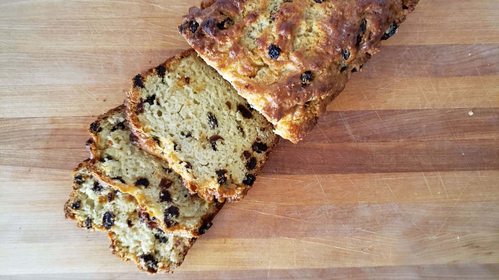 Overhead of a loaf of Irish soda bread on a wooden board with three slices cut next to it.
