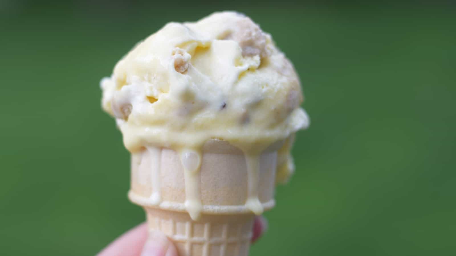 Melting cookie dough frozen custard in a standard cone with a green background.