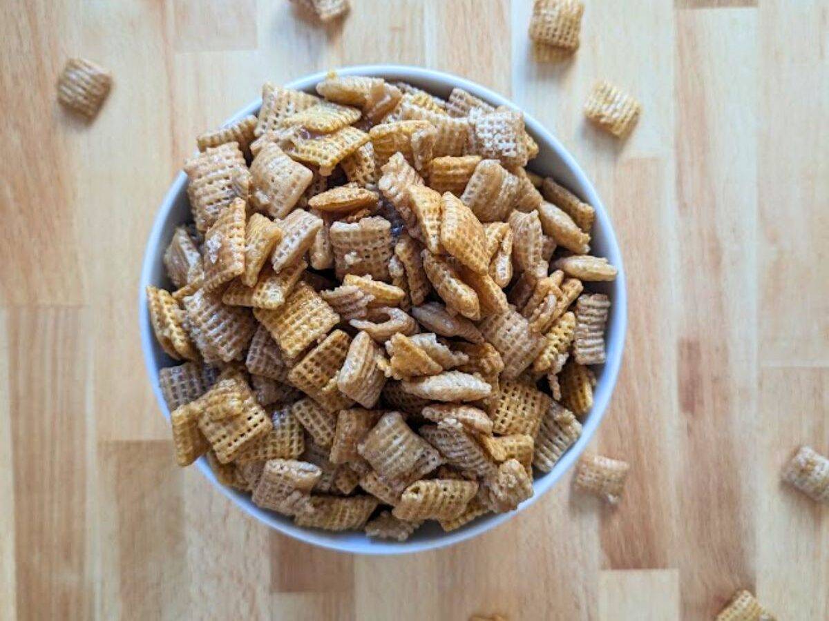 Overhead of a bowl of caramel chex mix with some scattered around it.