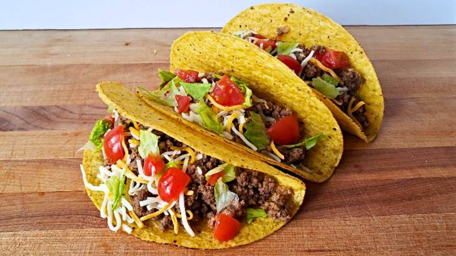 Three corn tacos sit on a wooden table filled to the brim with fillings.