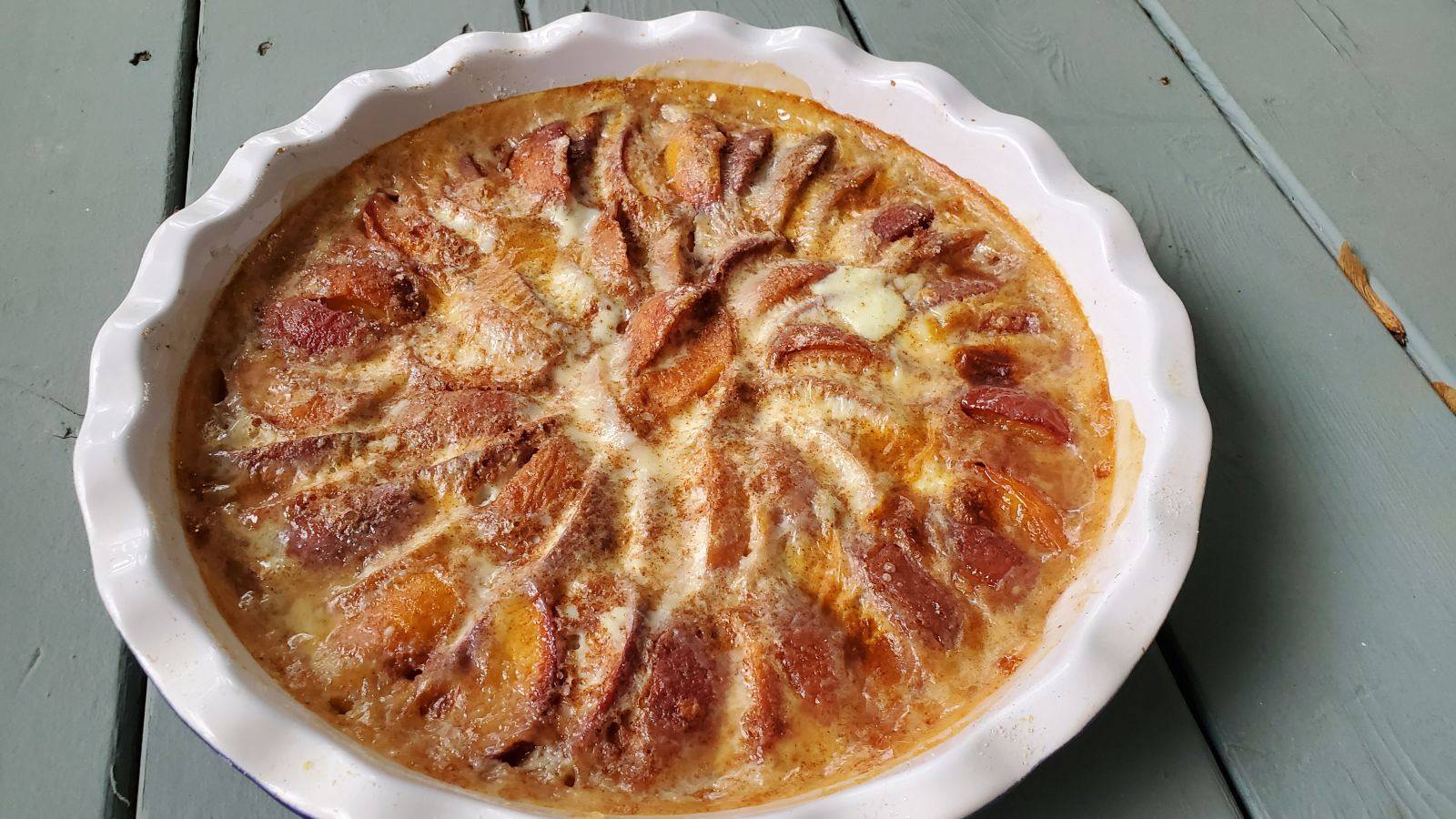 A pie pan filled with peach kuchen on a grey wooden table.