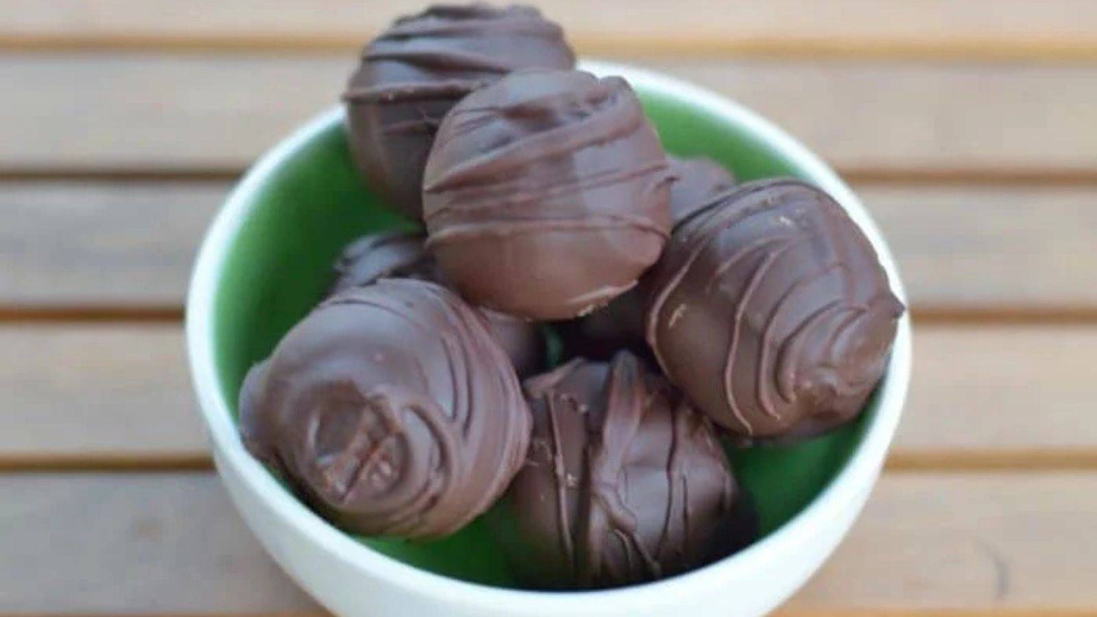 A bowl of cookie dough truffles stacked together and sitting on a wooden table.