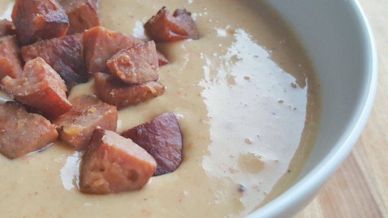 Closeup of a bowl of cheesy soup with chunks of sausage floating on top.