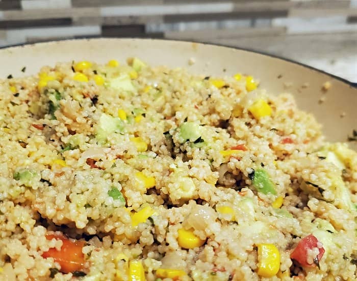 Close up of a pot of vegan couscous salad on a counter with a tiled backsplash.