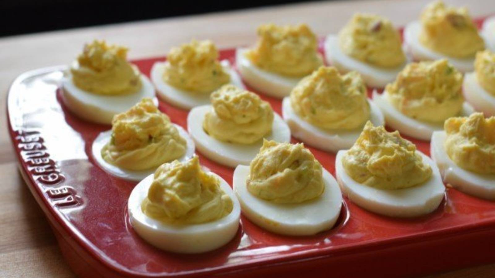 A red platter holds a series of bacon deviled eggs.