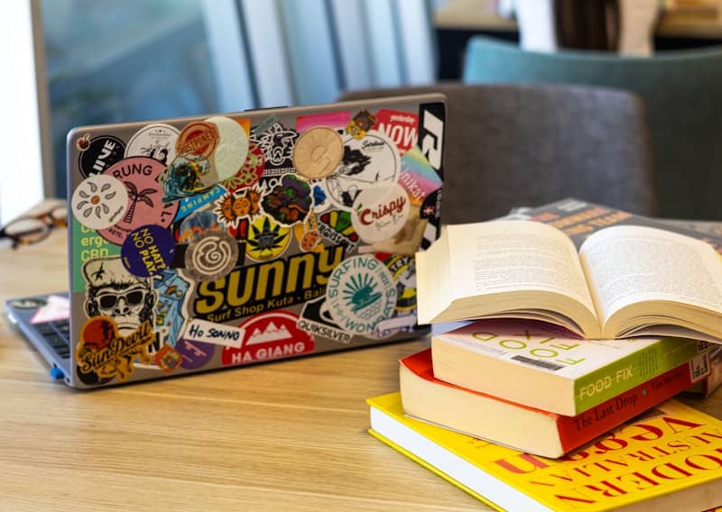 Laptop and books sit on a wooden table.