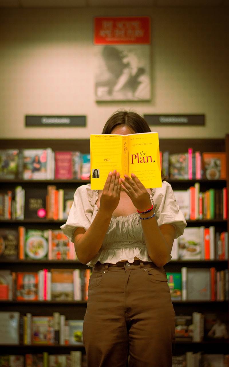 Woman holding a yellow book in front of her face.