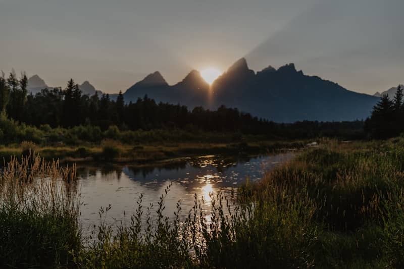 Sunrise behind jagged mountains over a serene lake