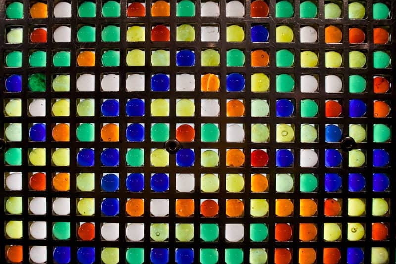 A grid of colorful glass marbles backlit in a dark metal frame