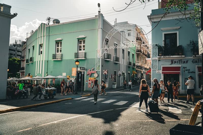 People walk on a sunny street with colorful buildings.