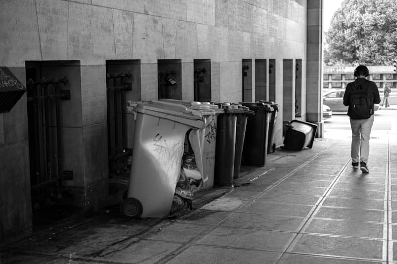 A broken trash bin is overturned, and a person walks by.