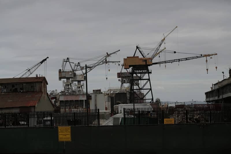Construction cranes at a shipyard under cloudy sky.