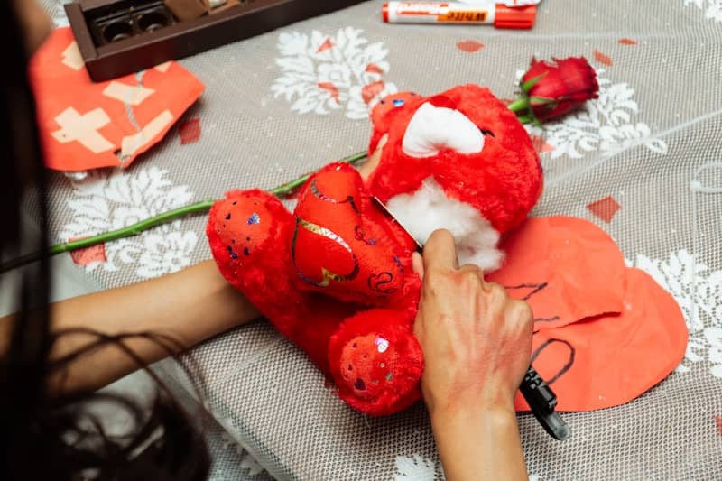 Person disassembling a red teddy bear with a knife