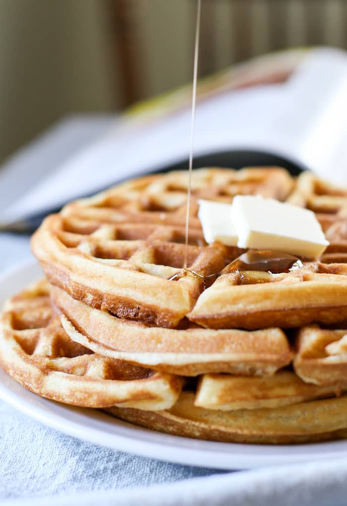 syrup being poured on waffles topped with butter
