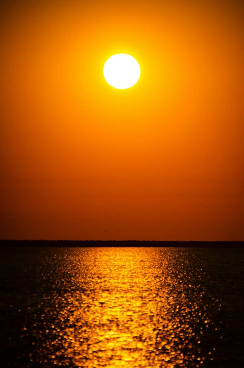 Golden sun setting above a shimmering ocean horizon.