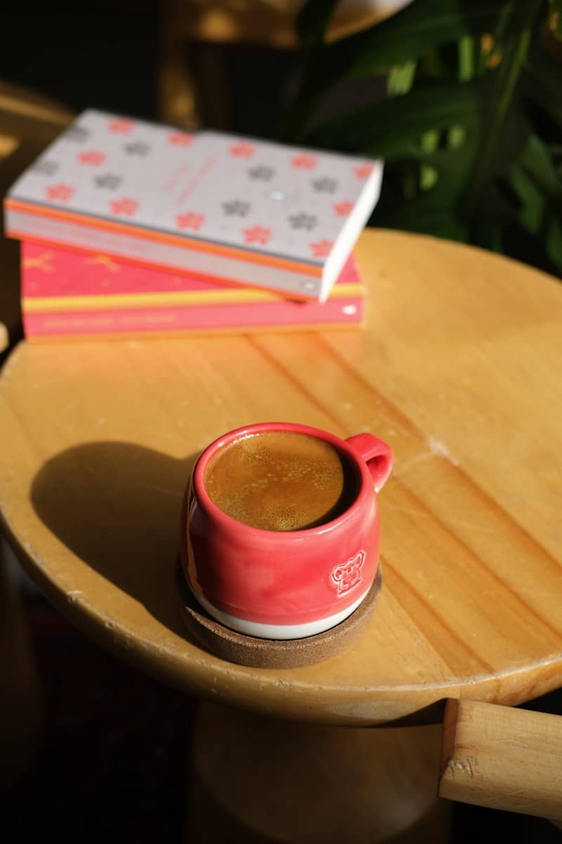 Red mug of coffee next to books on wooden table
