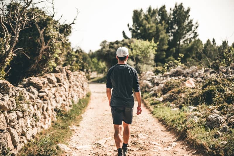 man walking on road between trees during daytime