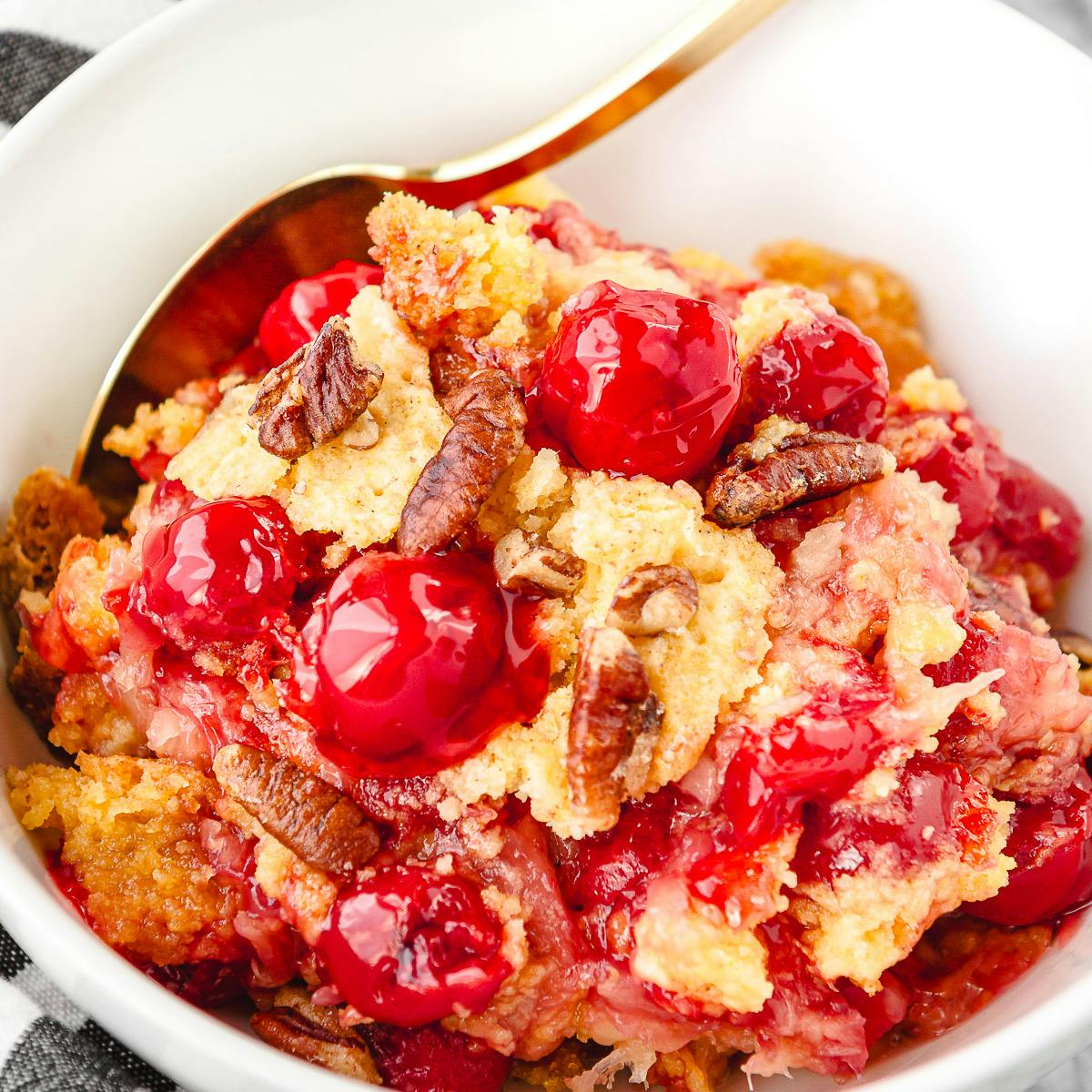 cherry pineapple dump cake in a white ceramic bowl with a gold spoon