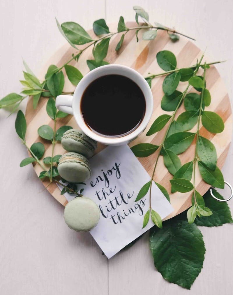 flat lay photography of leaves with cup of coffee and three macarons on chopping board