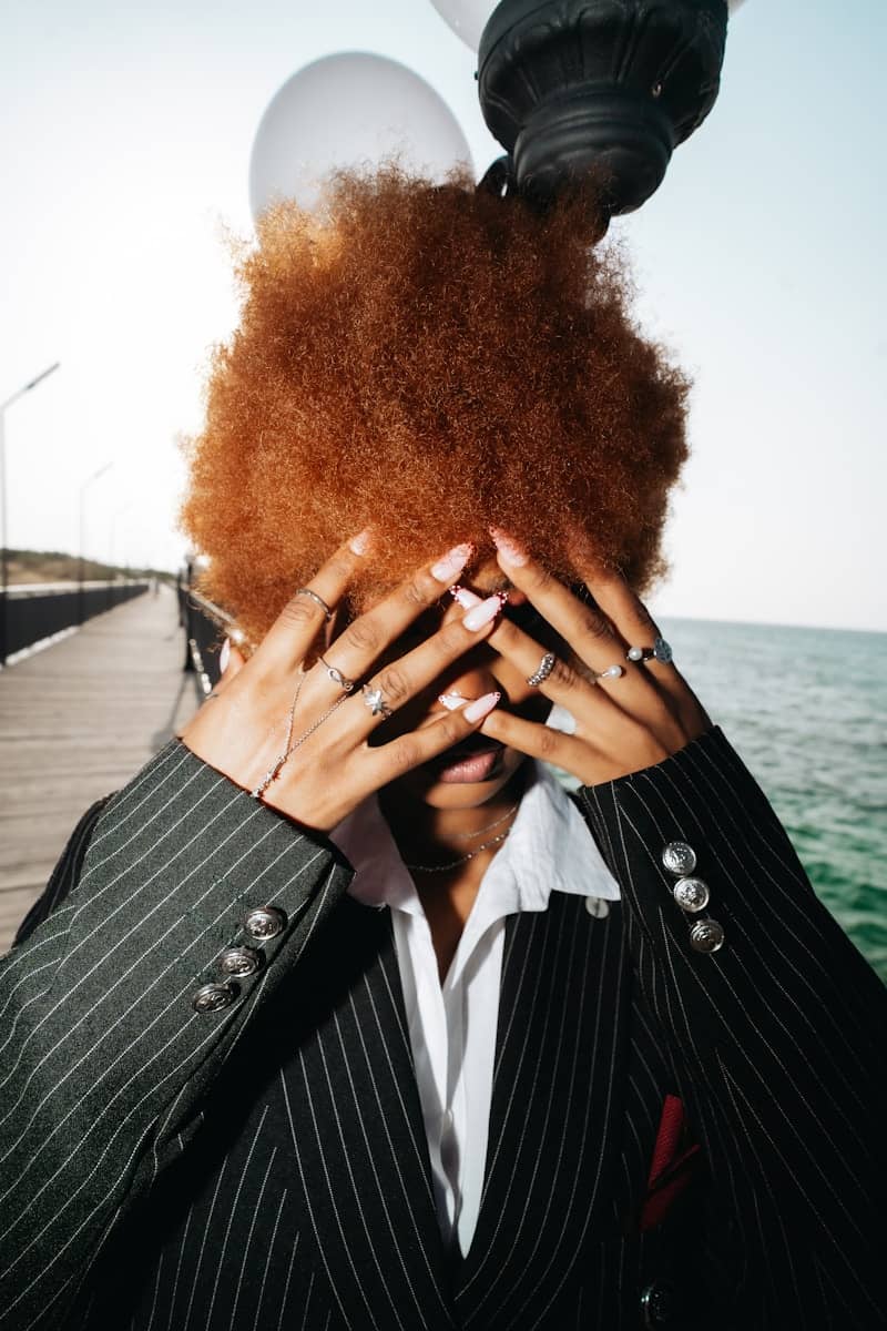 A person with ginger hair covering their face with hands on a wooden pier