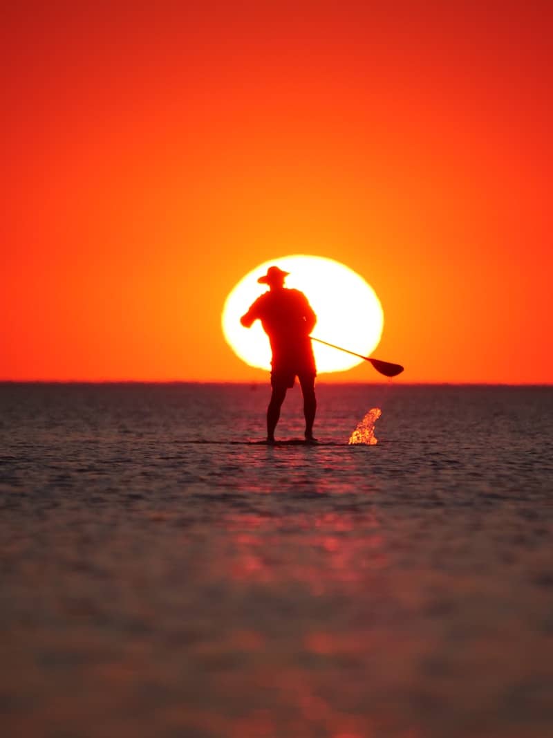 Man paddleboarding against a vibrant sunset