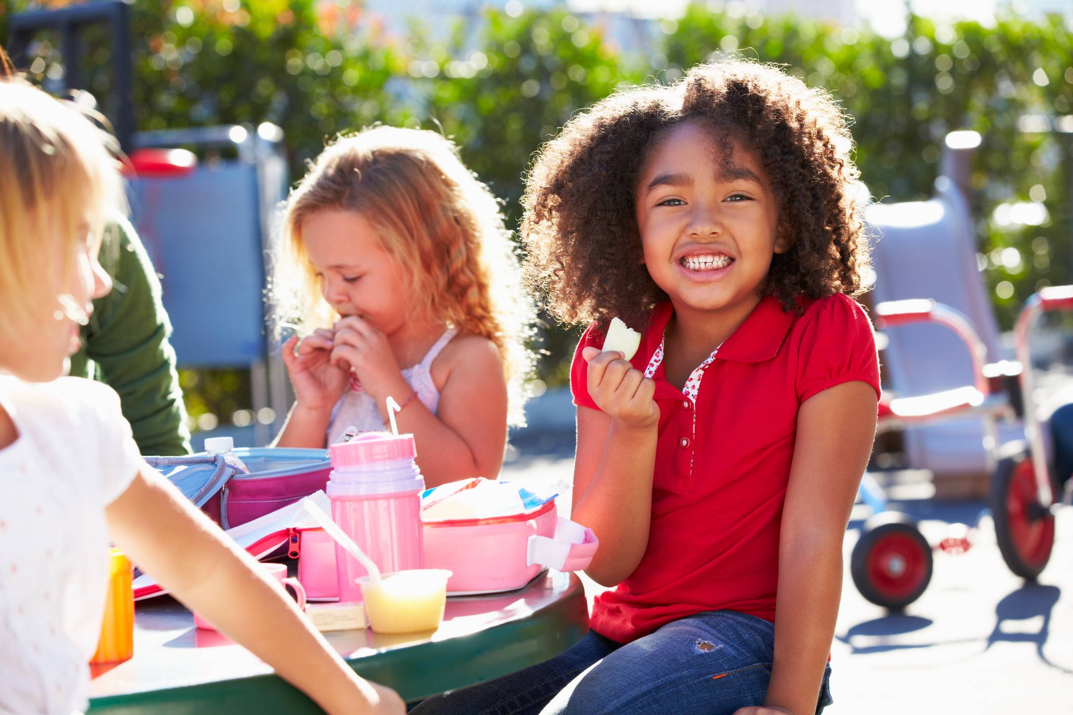 Children eating snacks together at an outdoor summer picnic table.