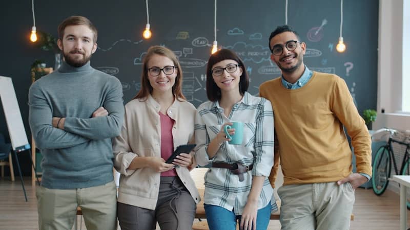 Four smiling people standing in a modern office.
