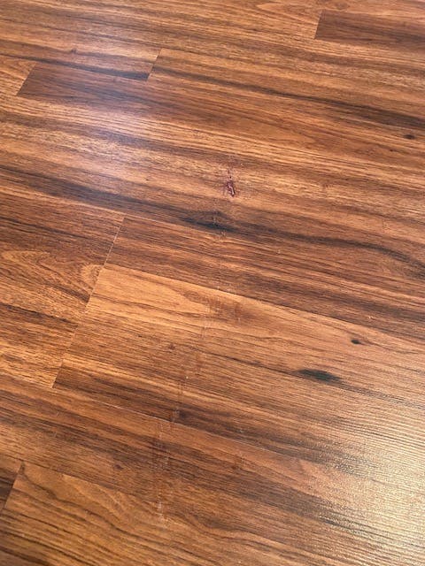 Photo shows brown laminate flooring where the white gouges have been covered up using a Mohawk Fil Stick. You cannot see where the markings are.