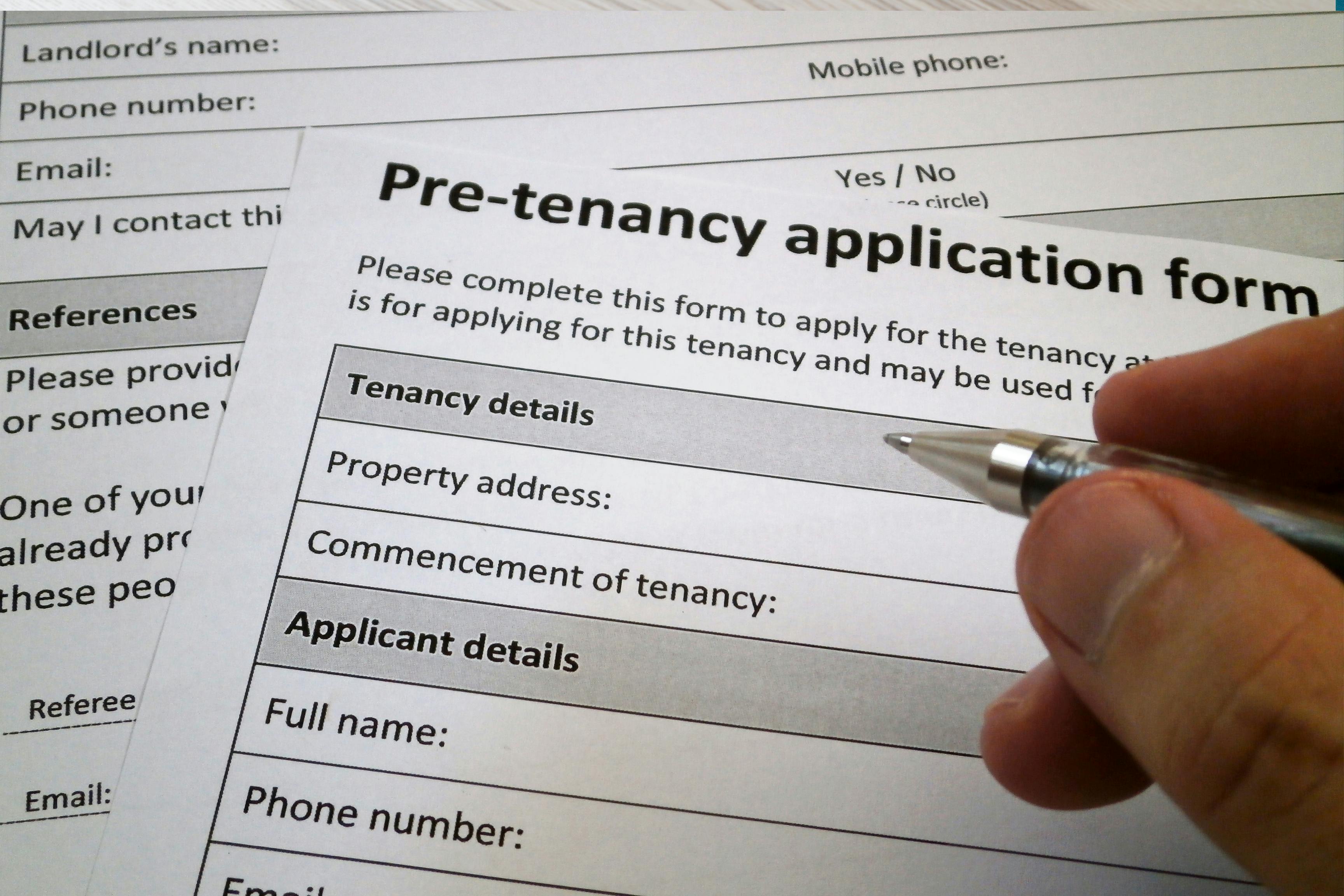 The image shows two forms lying on a desk. On the right side are a man’s fingers holding a pen about to fill out the top form.  The form is titled, Pre-tenancy application form. It asked that the form be completed, with such questions as, Tenancy details, Property address, Full name, Phone number, etc. Underneath this application is another form with questions related to references and landlord information.  The image conveys 5 professional tenants tactics and how to avoid them.