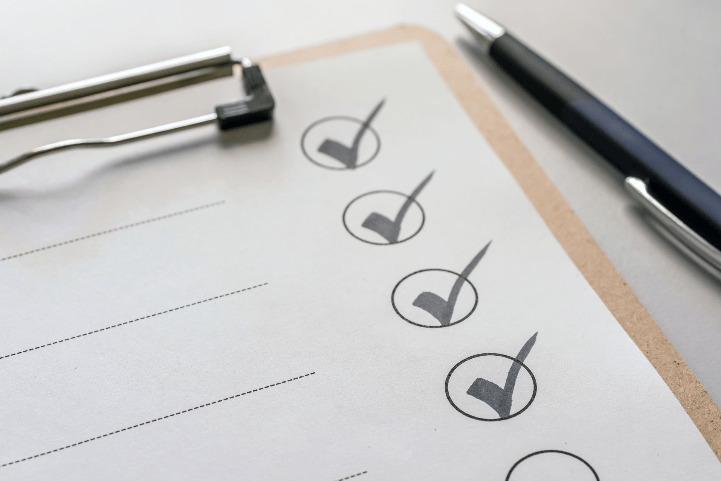 The image shows a clipboard with a pen next to it. A checklist is attached and four circles with checkmarks. The image conveys The Landlord’s Checklist for High Tenant Retention and Demand.