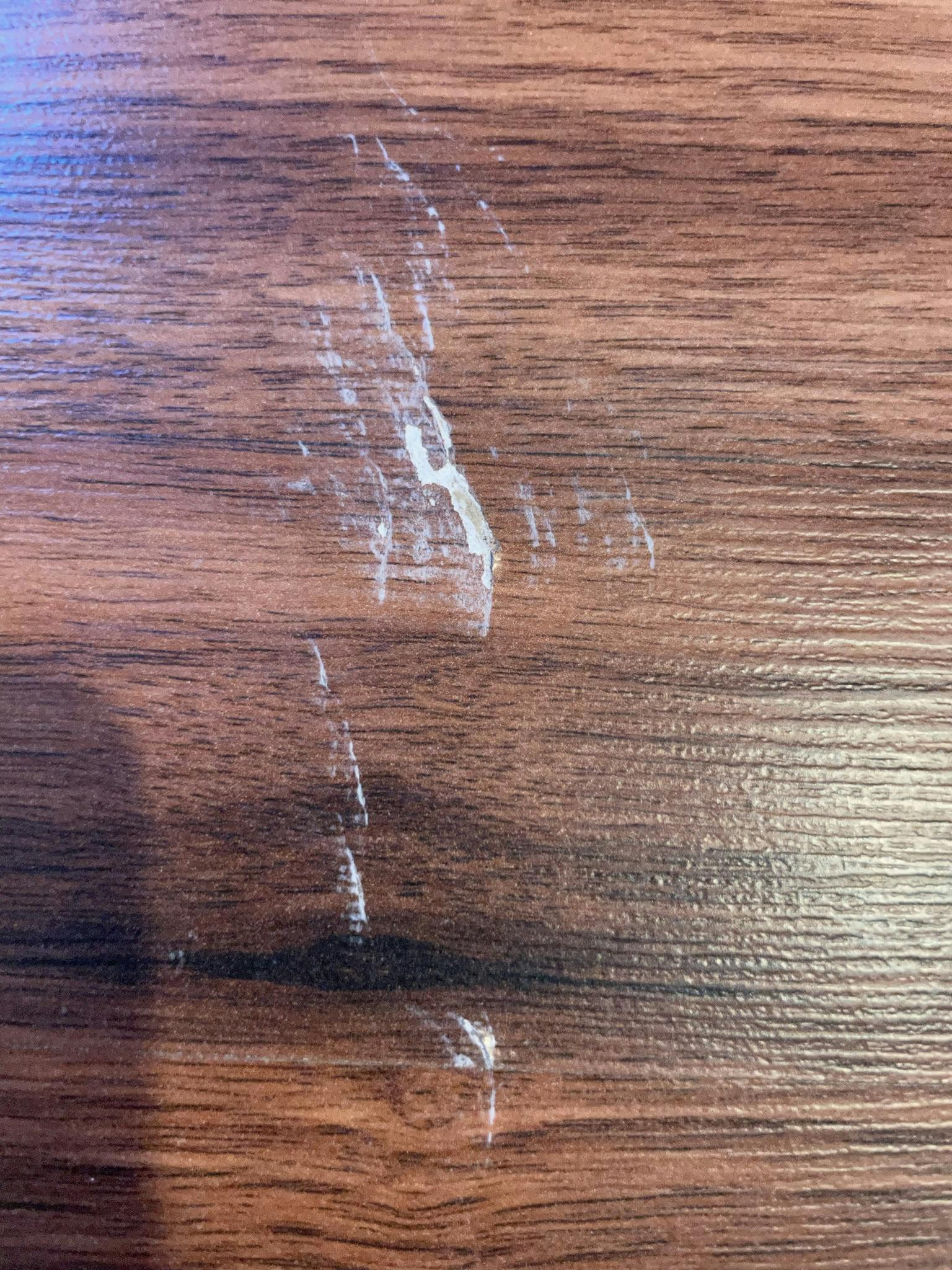 Photo shows a brown laminate wood grain floors with white scratches and gouges in it.