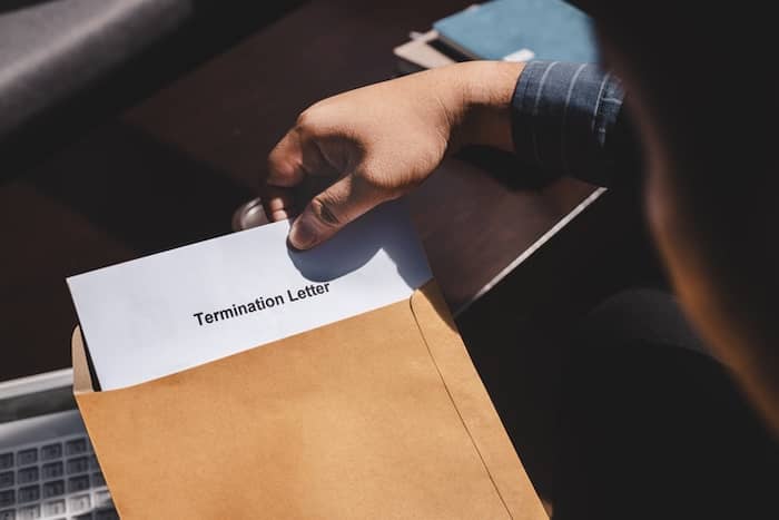 The image shows a hand removing a page from a yellow envelope. On top of the page is written Termination Letter. The image conveys How to Terminate Your Property Management Contract in 6 Steps.