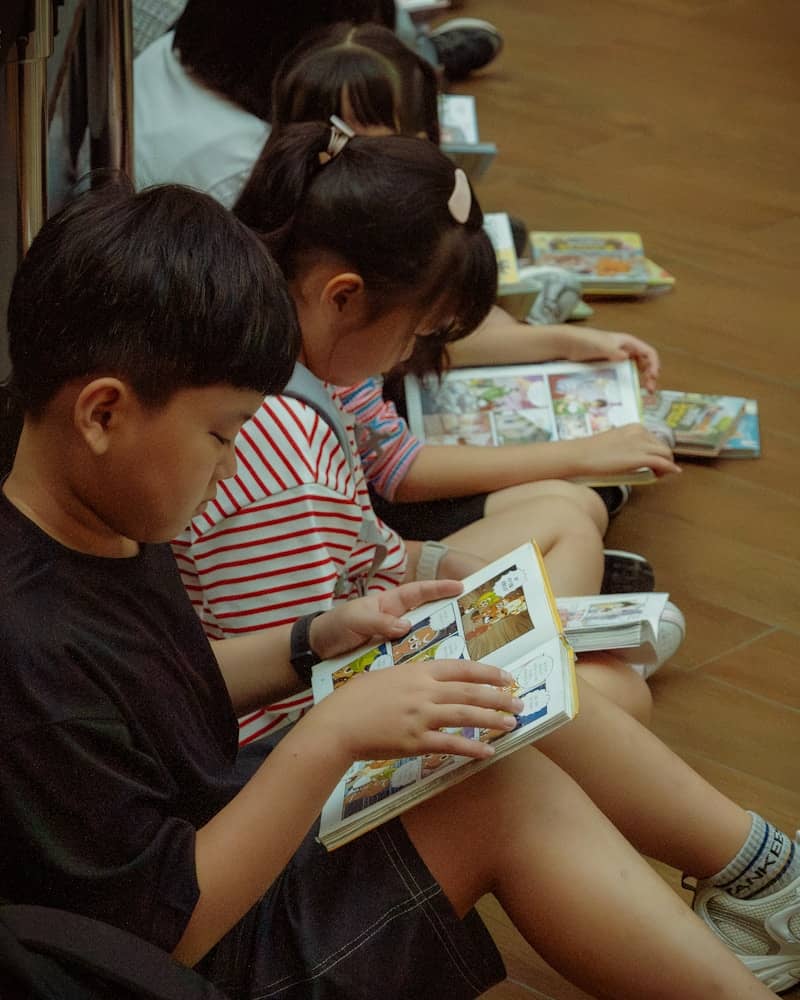 Young children quietly read comic books on the floor.