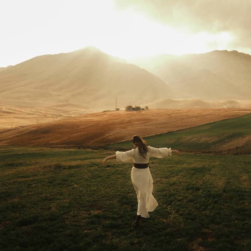Woman in white dress in a grassy field with mountains