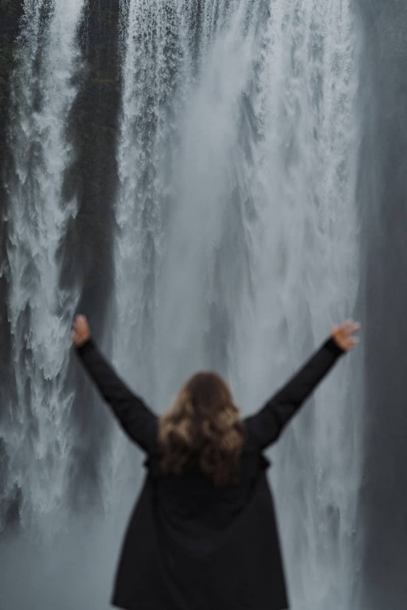 Woman stands before a beautiful, powerful waterfall.