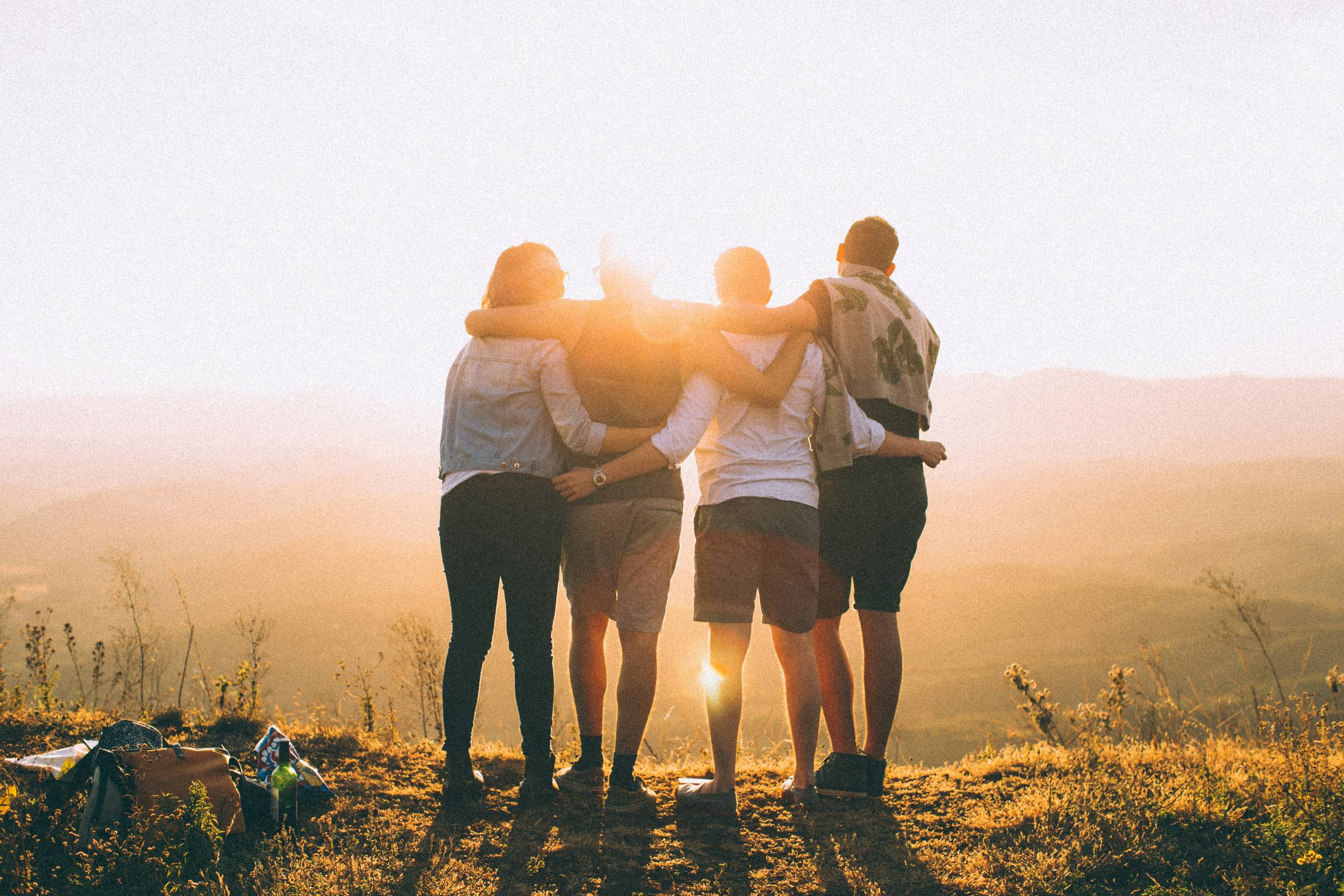 Four friends with arms around each other as the sun comes up