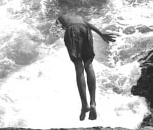 Person jumps from rocky cliff into turbulent ocean waves