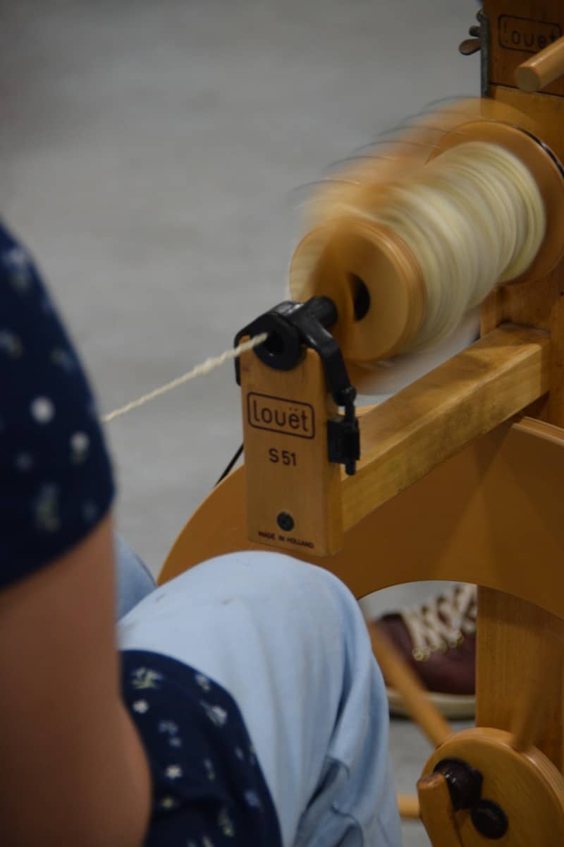 A person spinning yarn on a wooden wheel