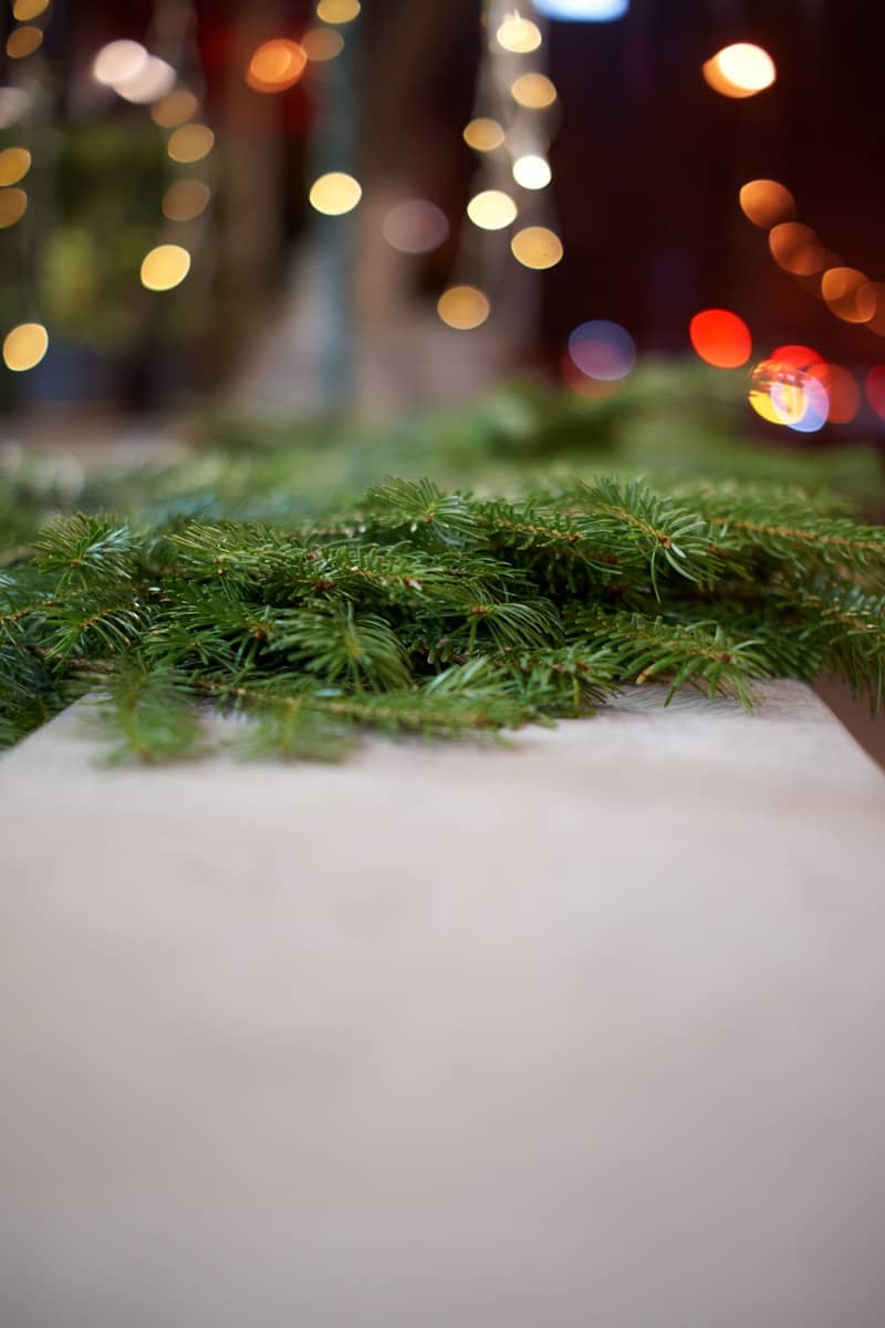 Green fir branches on a wooden surface with bokeh lights.