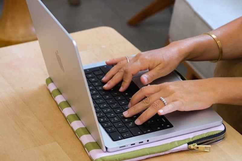 Hands typing on a laptop on a wooden table.