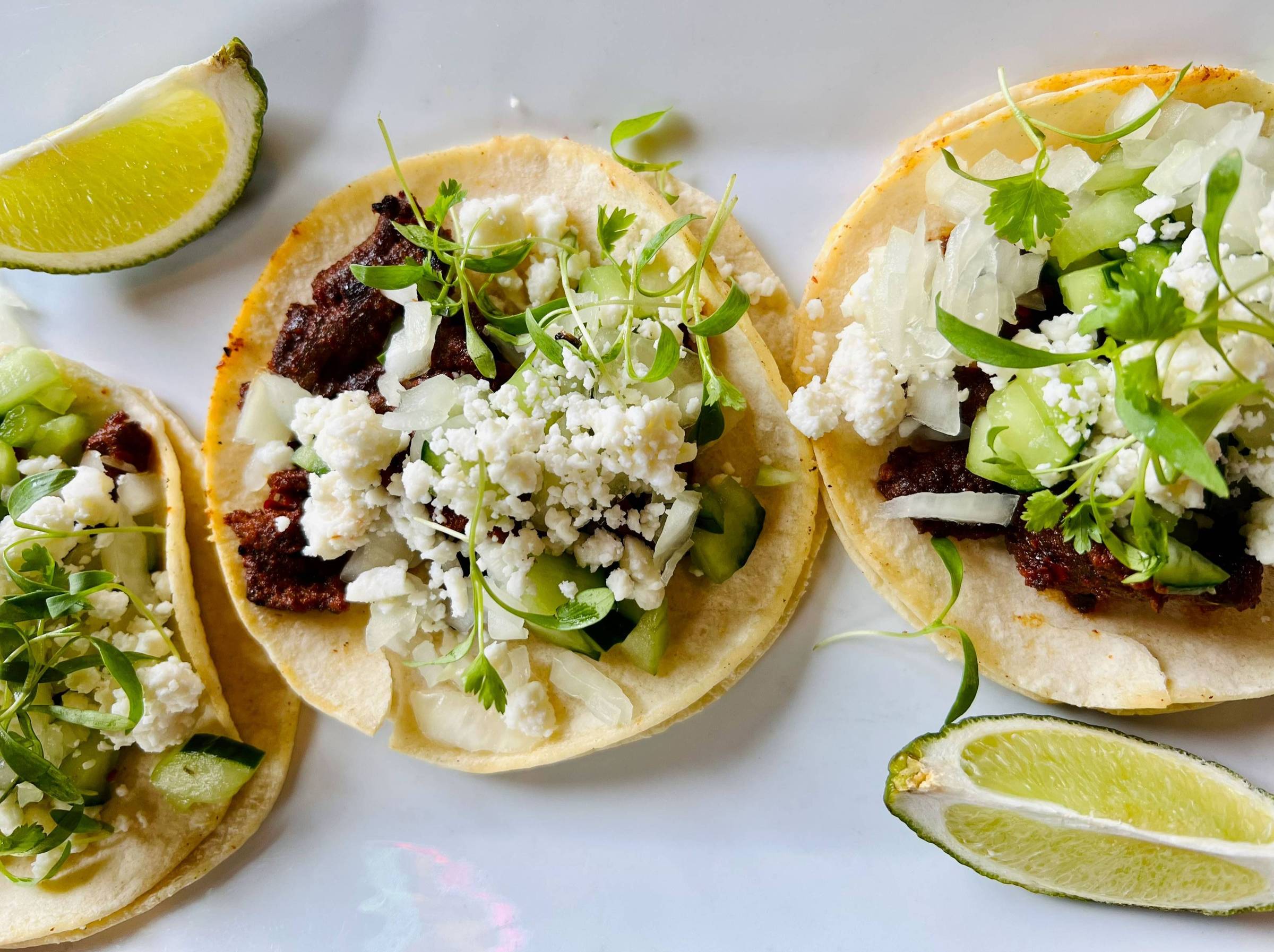 Street tacos on a white plate with limes