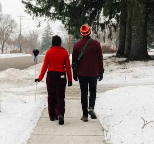 Two people walk on a snowy sidewalk in winter.