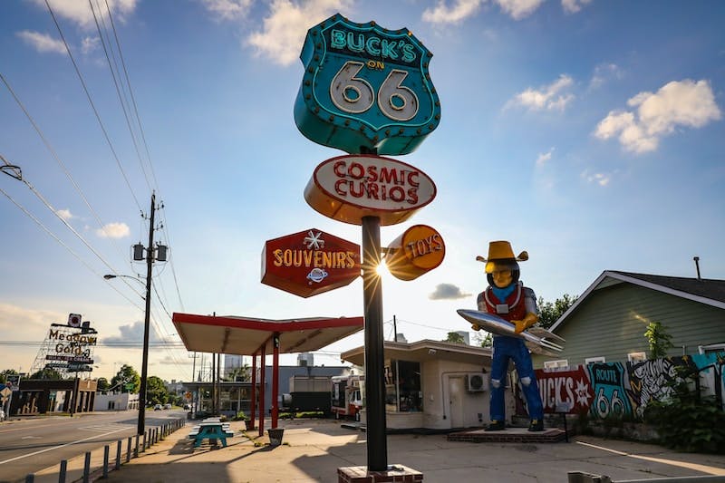 a statue of a cowboy holding a surfboard in front of a gas station