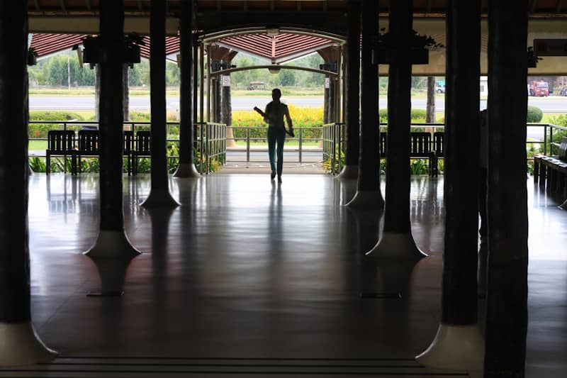 A person walks through a covered walkway with pillars.