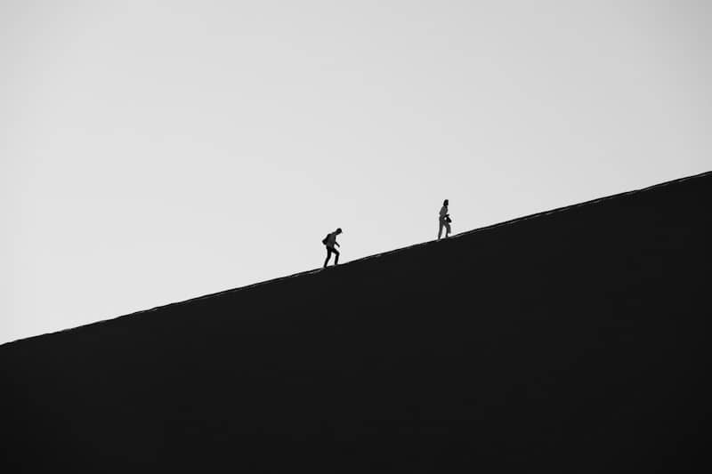 Two hikers ascend a dark, barren dune.